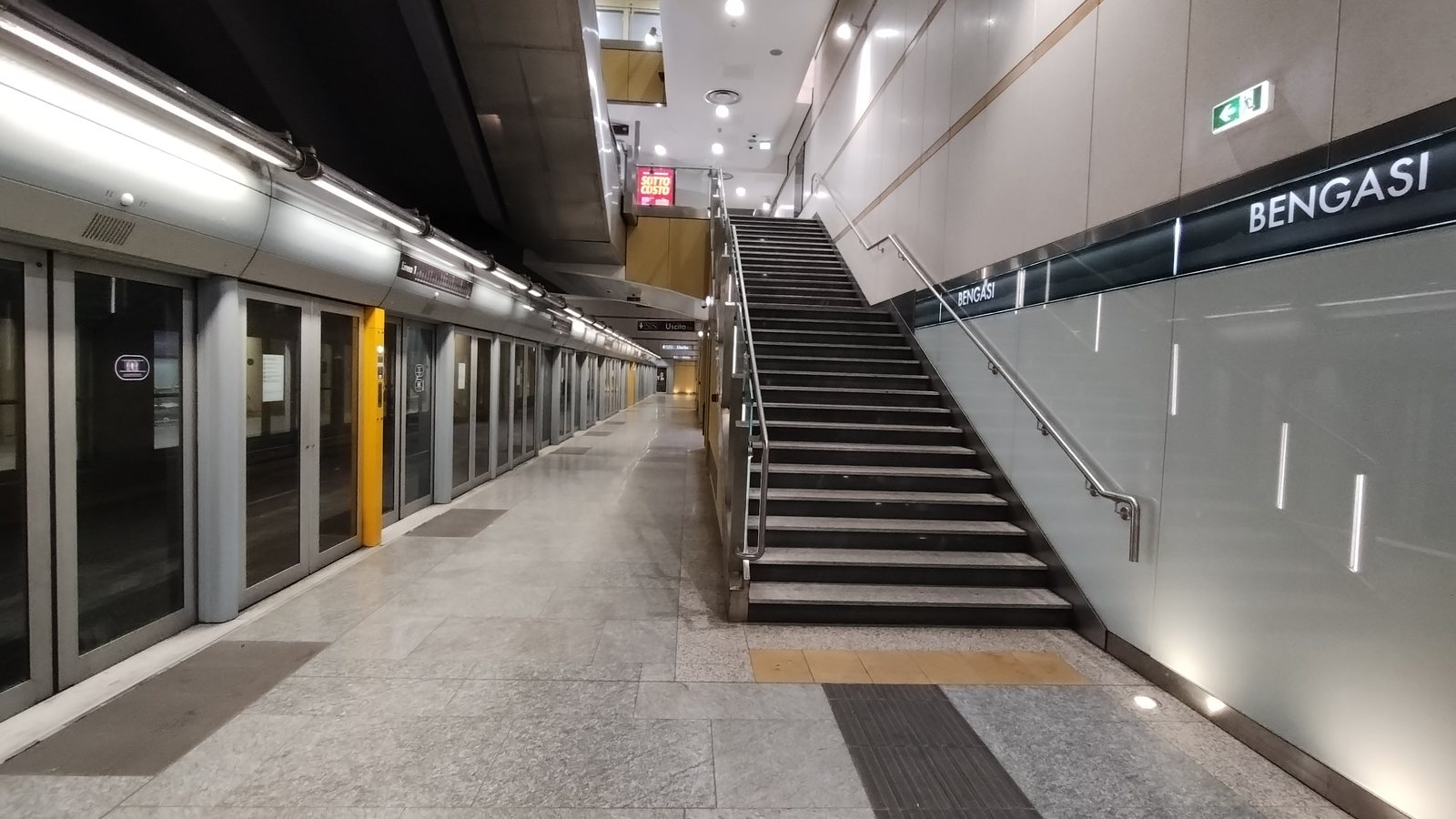 Treno fermo dietro le porte di banchina alla stazione Bengasi, con la targa BENGASI sulla parete