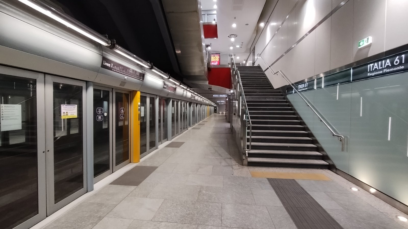 Treno fermo dietro le porte di banchina e targa ITALIA 61 REGIONE PIEMONTE sulla parete