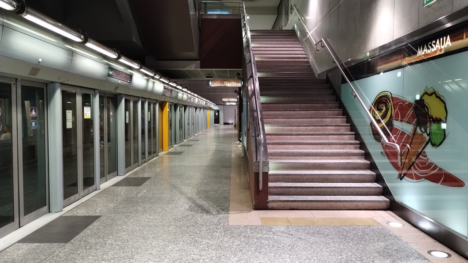 Treno fermo dietro le porte di banchina alla stazione Massaua, con la targa MASSAUA sulla parete