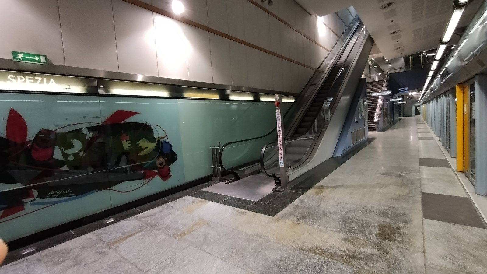 Targa SPEZIA, parete decorata e scala mobile sulla banchina della stazione Spezia