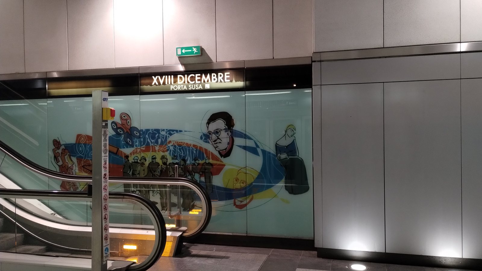 Targa XVIII DICEMBRE - PORTA SUSA sulla banchina, sopra la parete decorata e la scala mobile